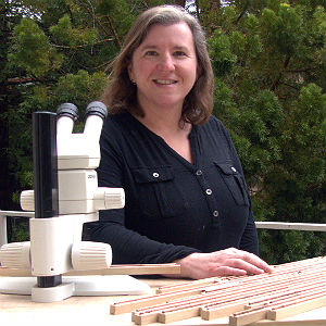 Allison Carroll, standing outdoors with microscope and tree samples