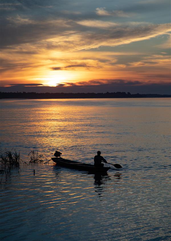 Medium_WW1194720-herenciacolombia Image of a person in a canoe on a wide river with a sunset in the background